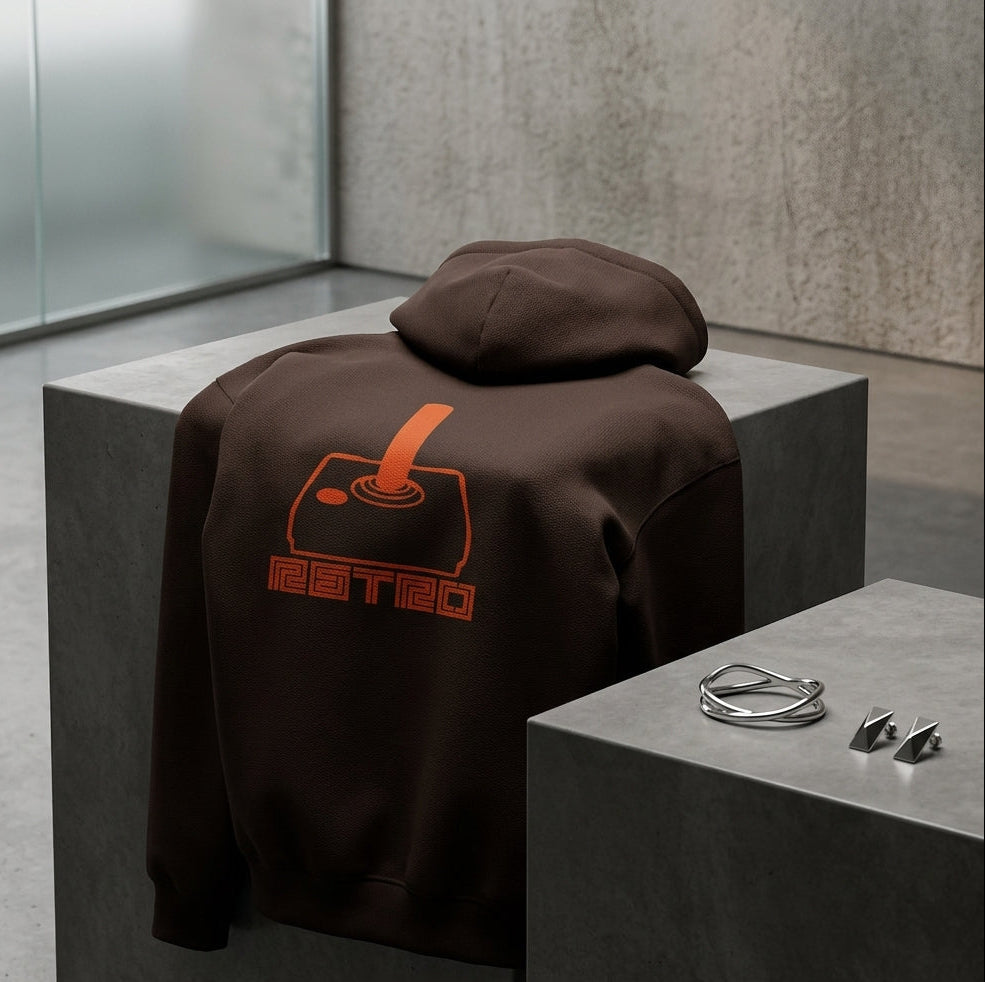 Brown Retro Arcade Joystick hoodie draped over a grey display block, showing an orange joystick graphic and retro lettering on the back.